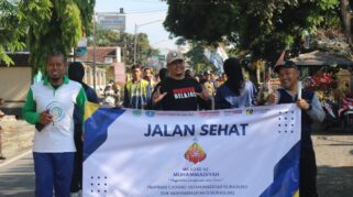 Sejumlah orang memegang spanduk bertuliskan "Jalan Sehat Milad ke-112 Muhammadiyah" sambil tersenyum.