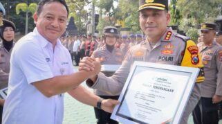 Seorang perwakilan dari Perhutani sedang menyerahkan piagam penghargaan kepada Kapolresta Banyuwangi. Keduanya terlihat tersenyum dan berjabat tangan.