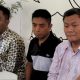 Tiga orang pria duduk di meja sambil melihat ke arah kamera