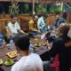 Foto menunjukkan sekelompok orang yang duduk di meja panjang di suatu kafe.
