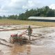 Seorang Babinsa sedang membantu petani membajak sawah dengan menggunakan traktor.