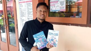Seorang guru memegang dua buku antologi cerpen berjudul "Ada Apa di Balik Layar Ponselmu?" dan "Fragmen Masa Remaja SMA".