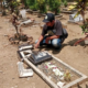 Seorang pria memeriksa nisan makam yang rusak dan berserakan.