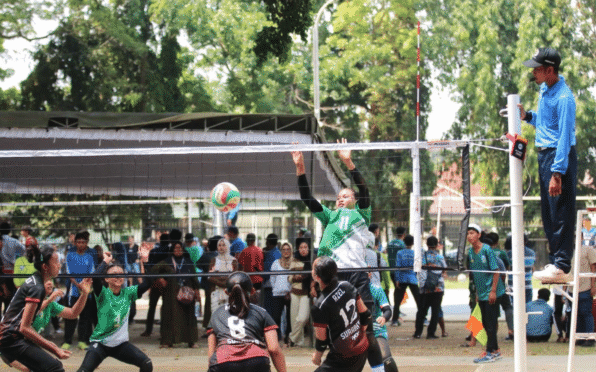 Tim Voli Putri Banyuwangi sedang bermain di lapangan voli. Salah satu pemain sedang melakukan smash, sementara pemain lain bersiap untuk menerima bola.
