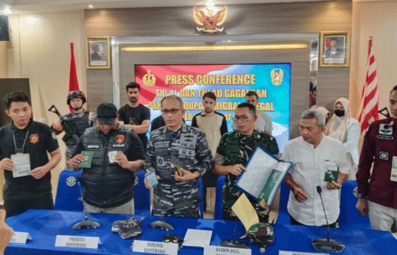Para petugas dari TNI AL dan kepolisian sedang memaparkan hasil penangkapan imigran gelap di sebuah ruangan. Terlihat sejumlah barang bukti yang diamankan, seperti paspor dan ponsel.