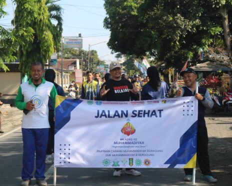Sejumlah orang memegang spanduk bertuliskan "Jalan Sehat Milad ke-112 Muhammadiyah" sambil tersenyum.