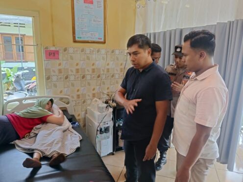 Gambar: Foto menunjukkan seorang pria sedang berbicara dengan seorang petugas polisi di sebuah ruangan rumah sakit. Terlihat seorang perempuan terbaring di tempat tidur di belakang mereka.