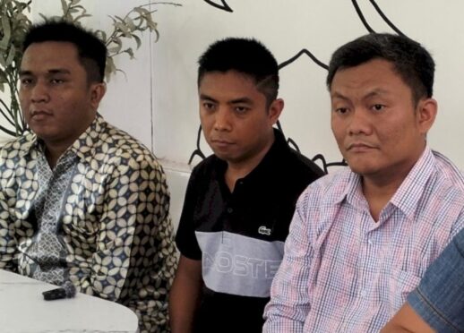 Tiga orang pria duduk di meja sambil melihat ke arah kamera