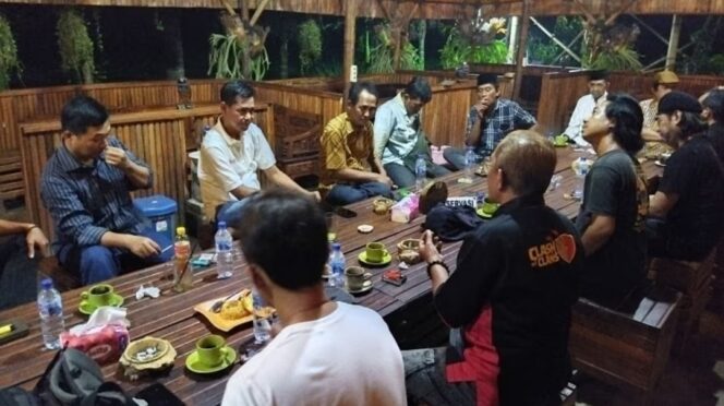 Foto menunjukkan sekelompok orang yang duduk di meja panjang di suatu kafe.