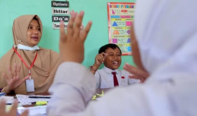 Seorang guru perempuan sedang menjelaskan materi pelajaran kepada siswa di kelas.