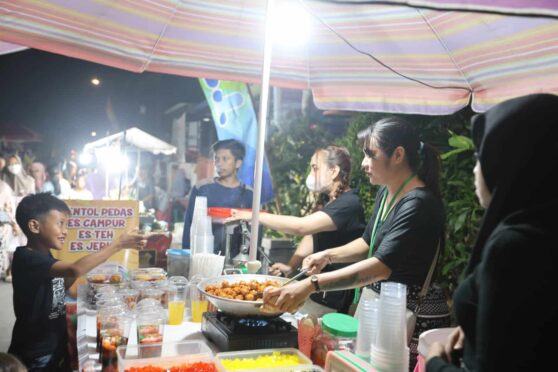 Seorang penjual sedang menggoreng makanan di sebuah stand makanan di Bazar Kuliner Kampoeng Cungking. Terlihat beberapa orang pengunjung yang antusias mendekat ke stand tersebut.
