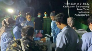Seorang polisi sedang menyelidiki lokasi kejadian di sebuah ruangan, dengan fokus pada sebuah benda kecil yang tergeletak di lantai.