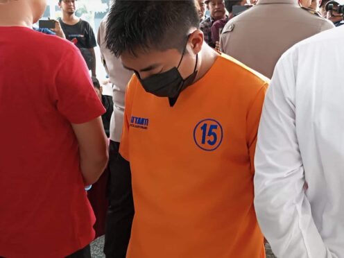 Seorang pria mengenakan baju tahanan berwarna orange sedang berdiri dengan tangan diborgol.