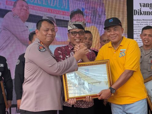Seorang perwakilan Polresta Banyuwangi sedang menerima penghargaan berupa piagam dari seorang perwakilan Harian Memorandum. Kedua pria tersebut sedang berjabat tangan.