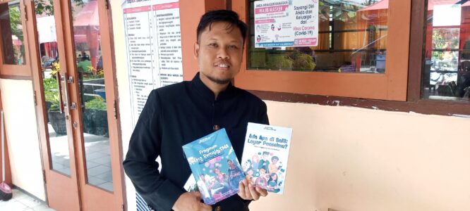 Seorang guru memegang dua buku antologi cerpen berjudul "Ada Apa di Balik Layar Ponselmu?" dan "Fragmen Masa Remaja SMA".