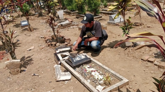 Seorang pria memeriksa nisan makam yang rusak dan berserakan.