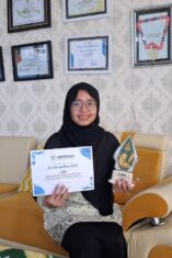 Cici Arista Devi menunjukkan piala dan sertifikat Juara I Lomba Menulis Artikel PDNA Banyuwangi di ruang prestasi SMK Muhammadiyah 8 Siliragung.