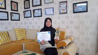 Cici Arista Devi menunjukkan piala dan sertifikat Juara I Lomba Menulis Artikel PDNA Banyuwangi di ruang prestasi SMK Muhammadiyah 8 Siliragung.